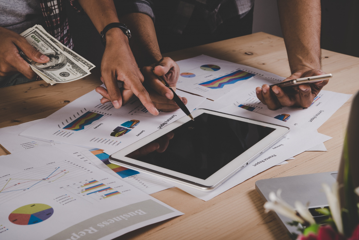 A close-up of professionals discussing financial data with charts and graphs, involving cash and digital devices for business research.