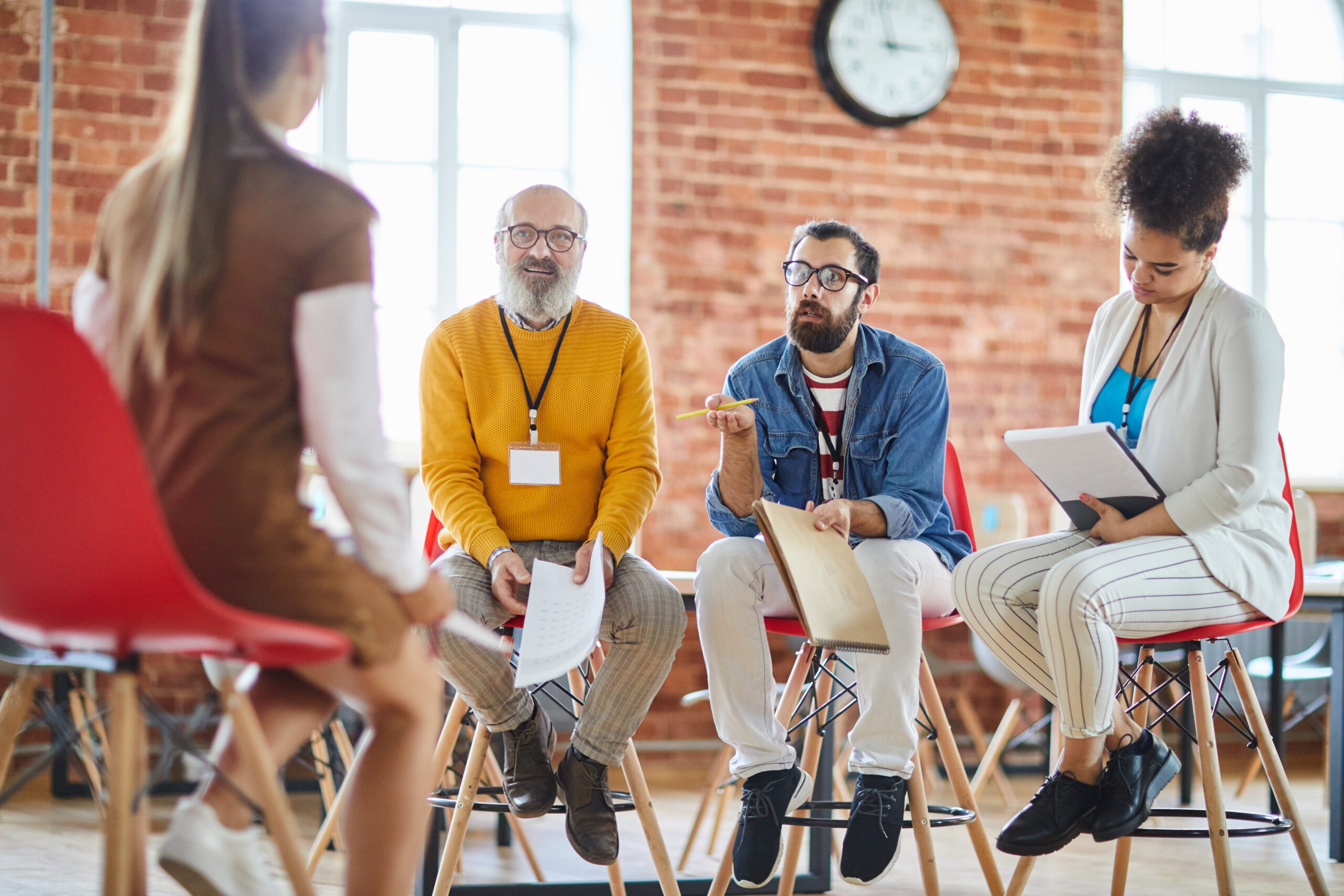 Alt text: Diverse group of four people discussing during an academic team meeting in a bright industrial-style office.