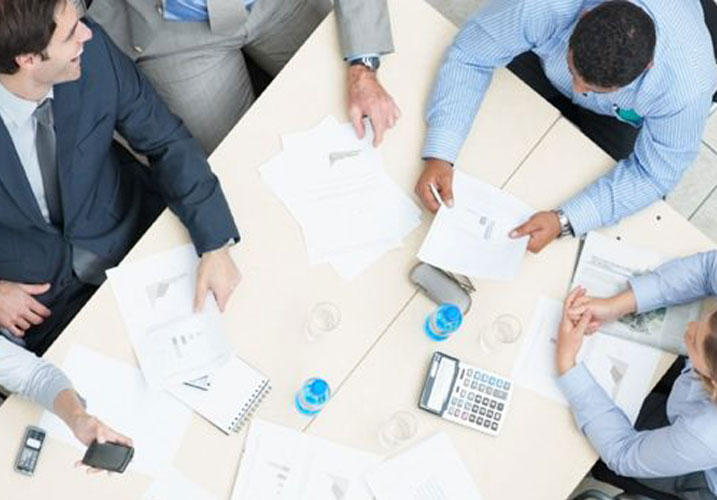 Business professionals discussing project reports and strategic planning around a conference table.