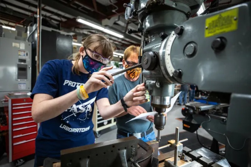High school students working on a science project using a microscope and industrial equipment.