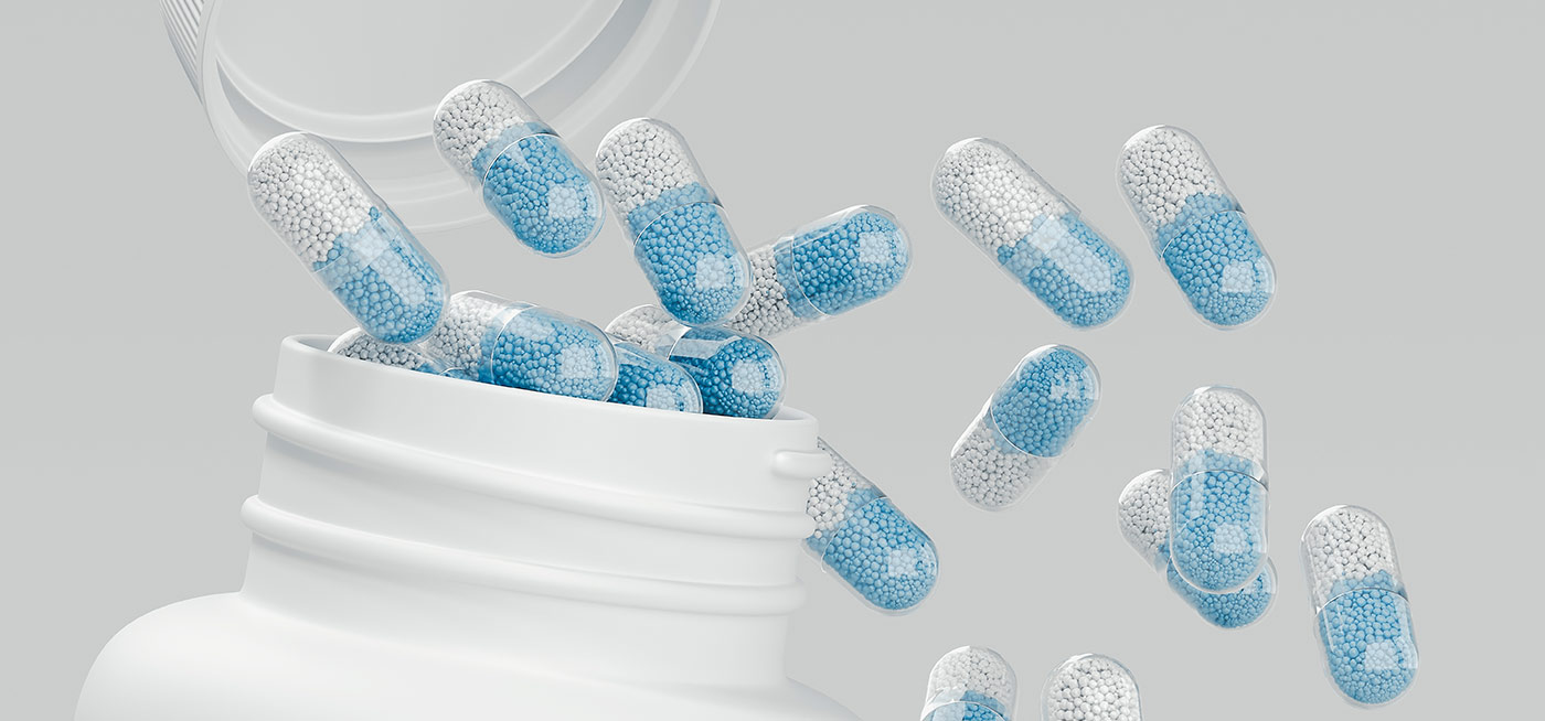 Close-up of capsules filled with white and blue microbeads spilling from a white bottle, illustrating pharmaceutical research.