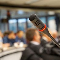 A researcher presenting findings at an academic conference with an audience in the background.