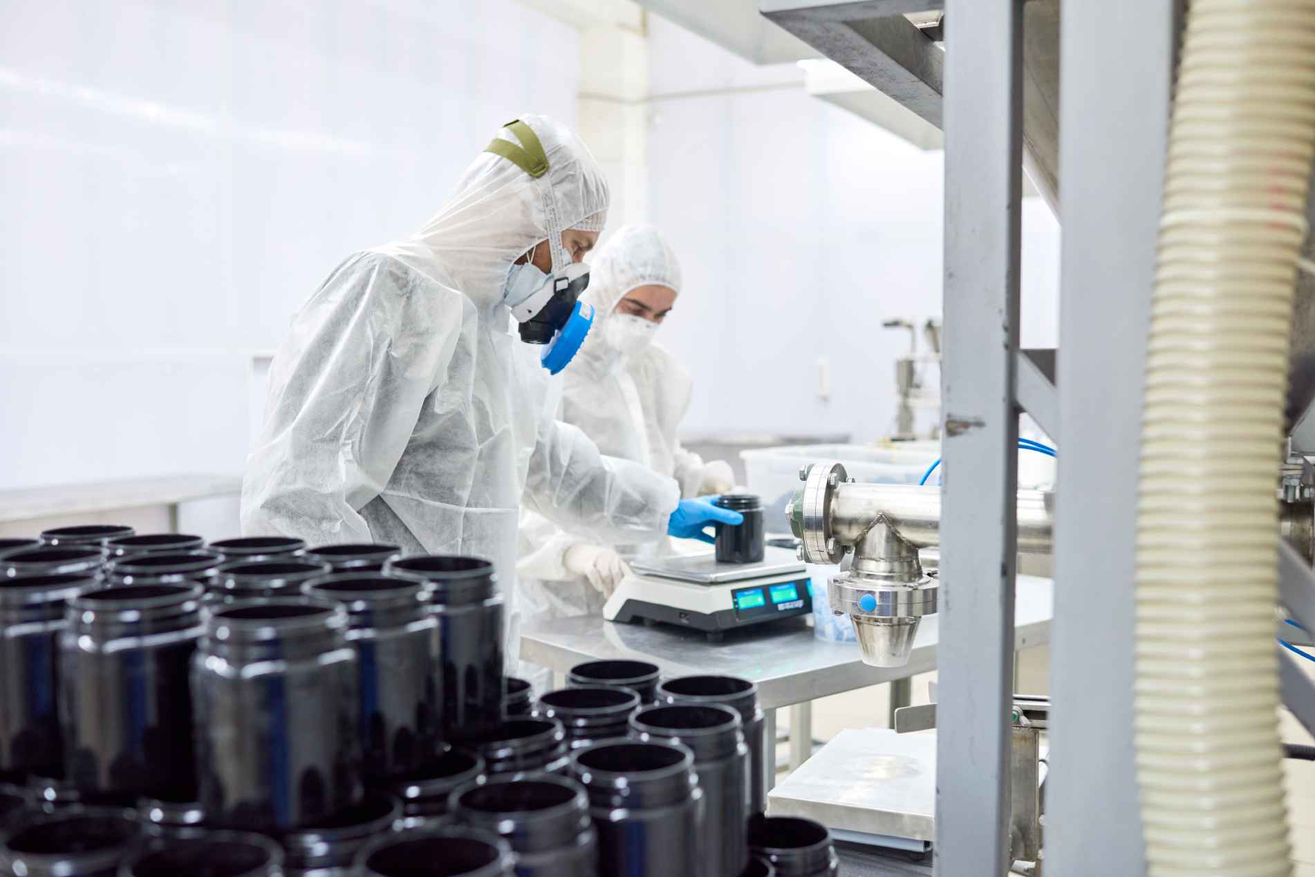 Laboratory scientists in protective gear conducting experiments using precision scales and machinery.