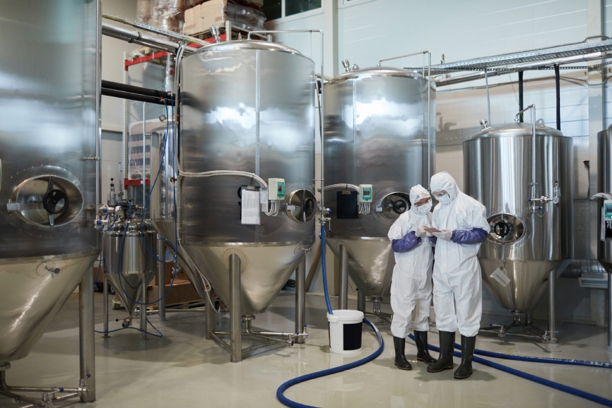 Stainless steel tanks in a brewery with two workers inspecting equipment.