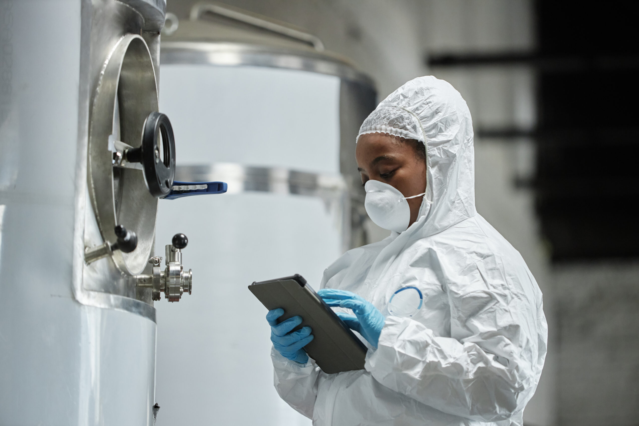 Scientist in protective gear using tablet in a modern laboratory environment.