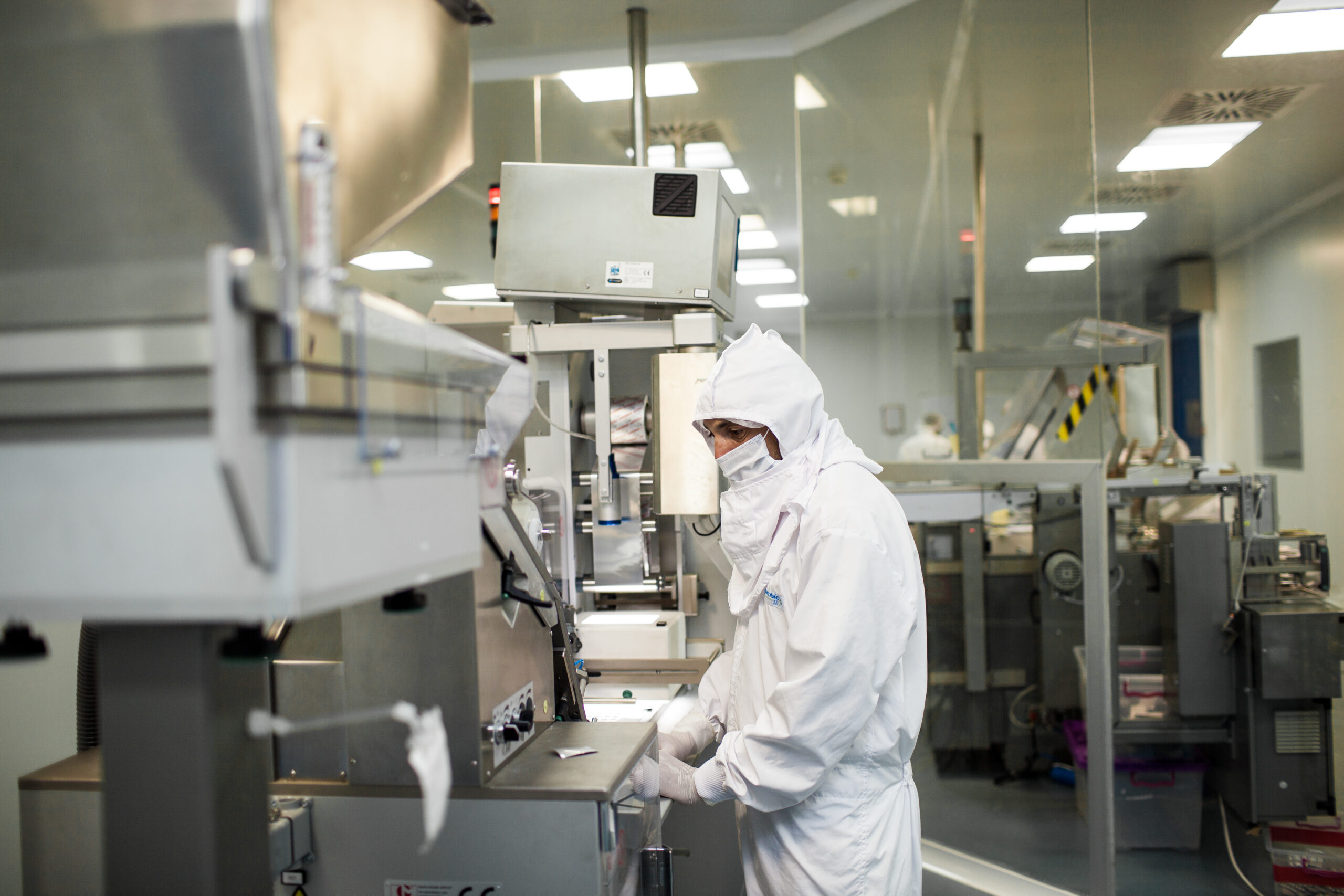 Laboratory technician in protective gear operating advanced pharmaceutical equipment in a cleanroom setting.