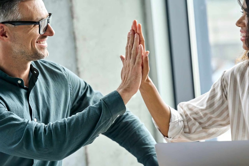 Two professionals giving a high-five during a discussion about FAQs.