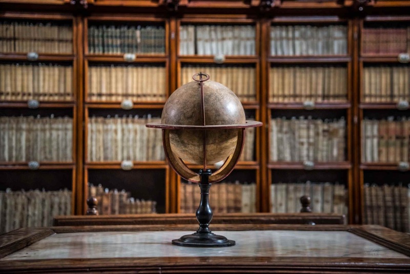 Historical globe displayed in front of a bookshelf filled with old books.