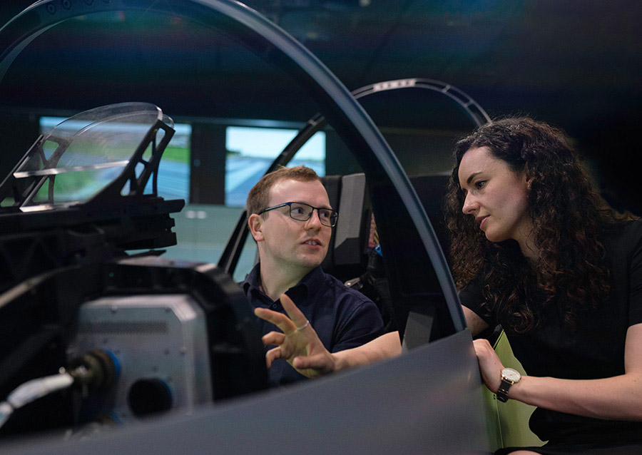 Detailed alt text: Two engineers discussing aircraft simulation in a high-tech aerospace testing facility.