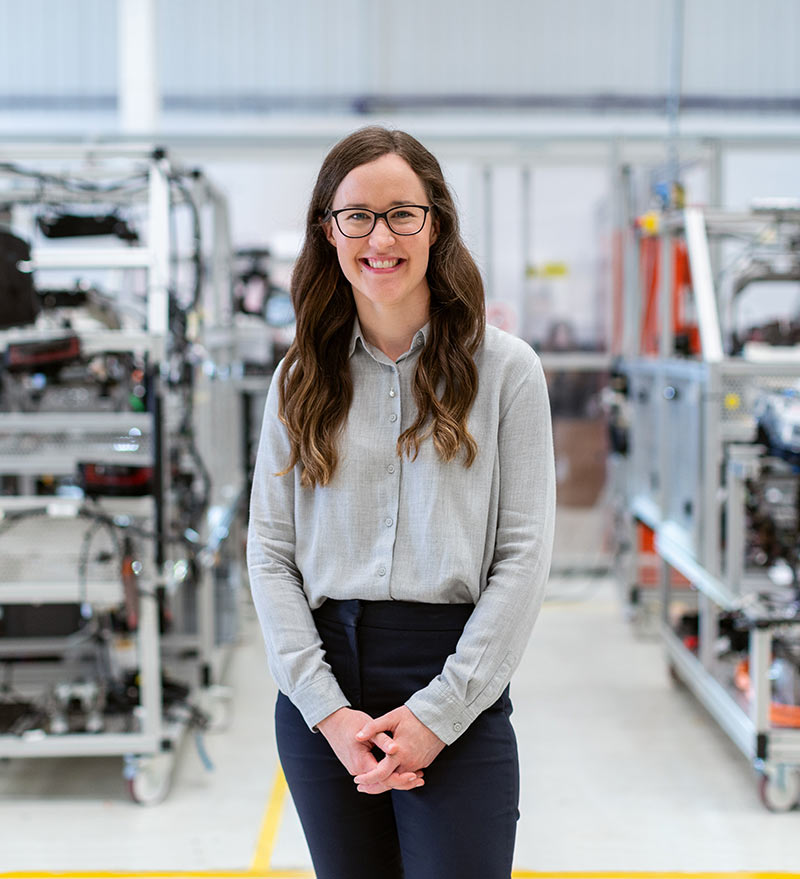 A smiling woman engineer in a laboratory surrounded by scientific equipment and machinery.