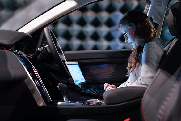 A woman using a laptop inside a car, highlighting research, technology, and innovation in automotive studies.