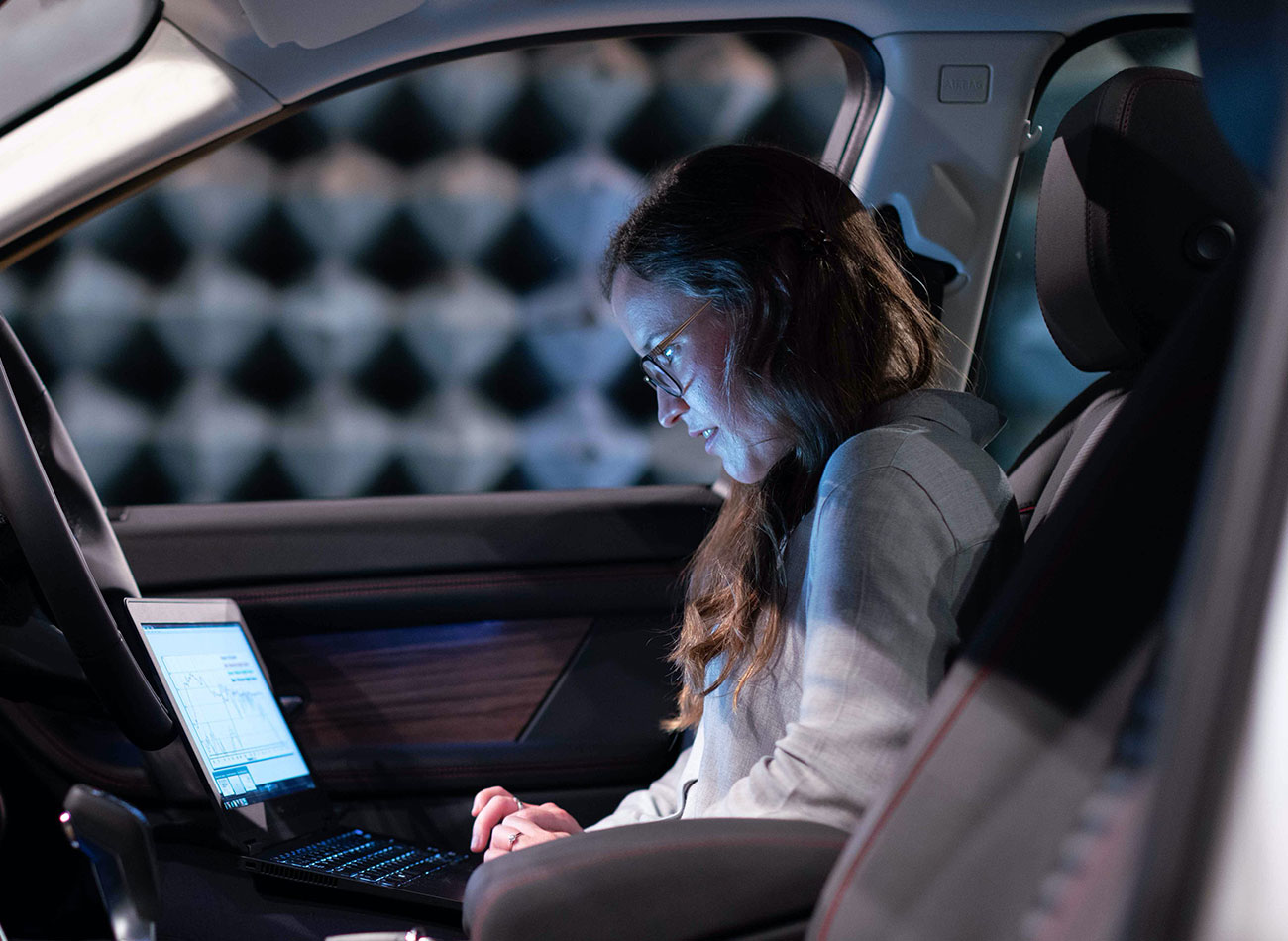 Young woman working on autonomous vehicle research with laptop inside car.