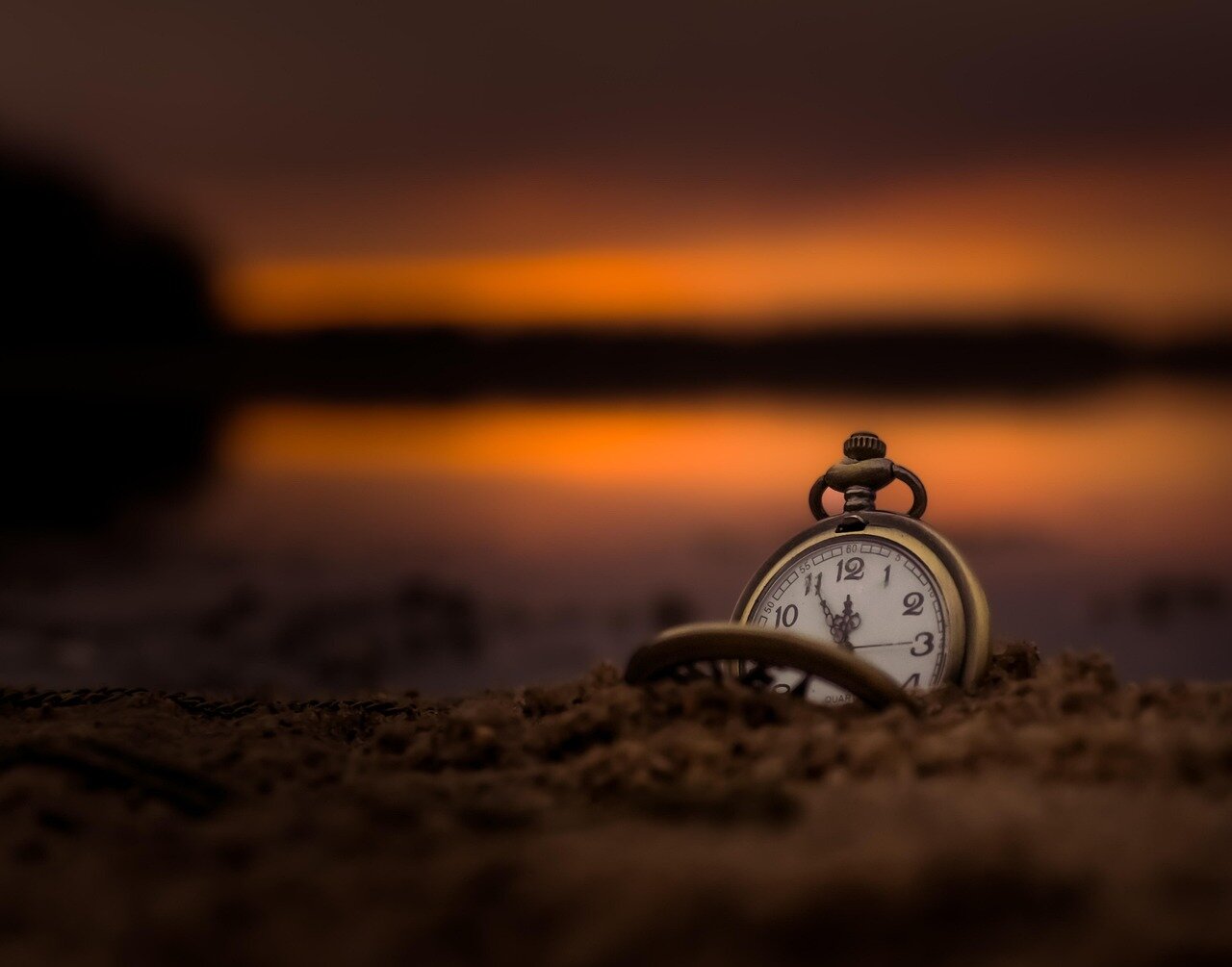 Vintage pocket watch on sandy surface during sunset, symbolizing time and mathematical flow.
