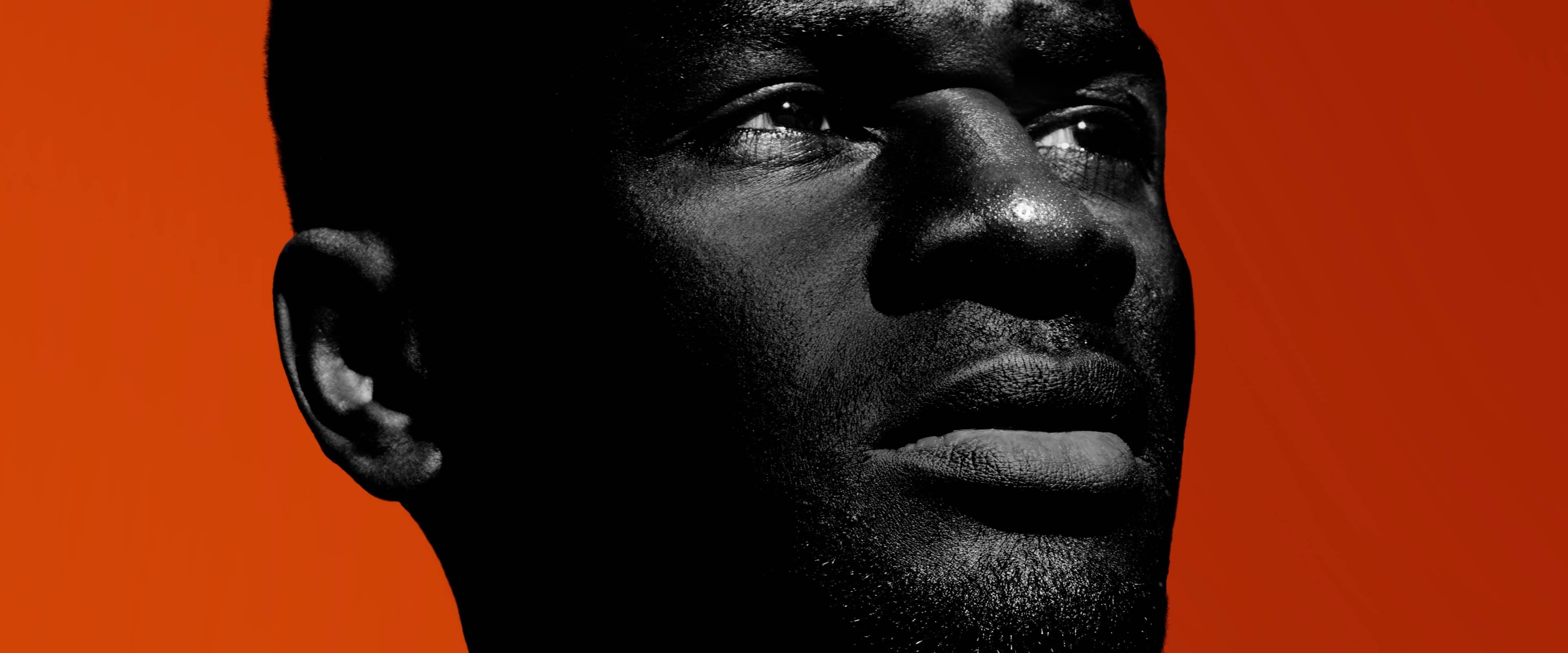 Close-up of black man's face with dark skin against orange background for social science research.
