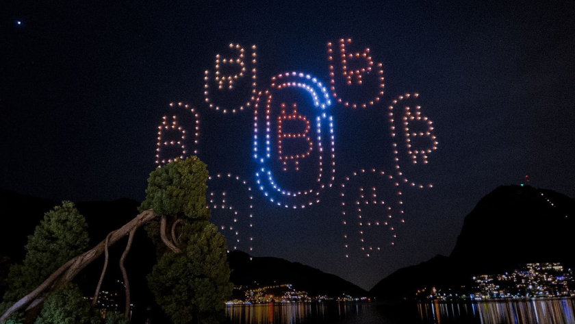Drone light display of a hope symbol at night with mountains and water reflections.