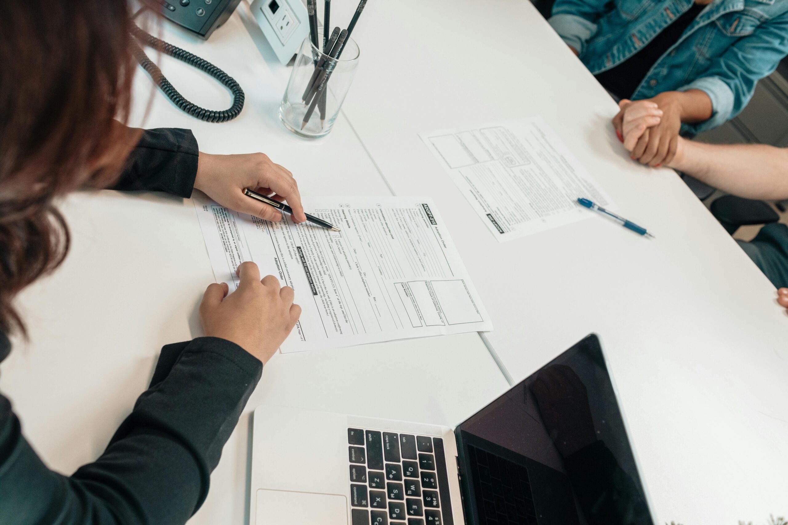A person reviewing and signing a research grant application form at a white table with a laptop, pens, and documents.