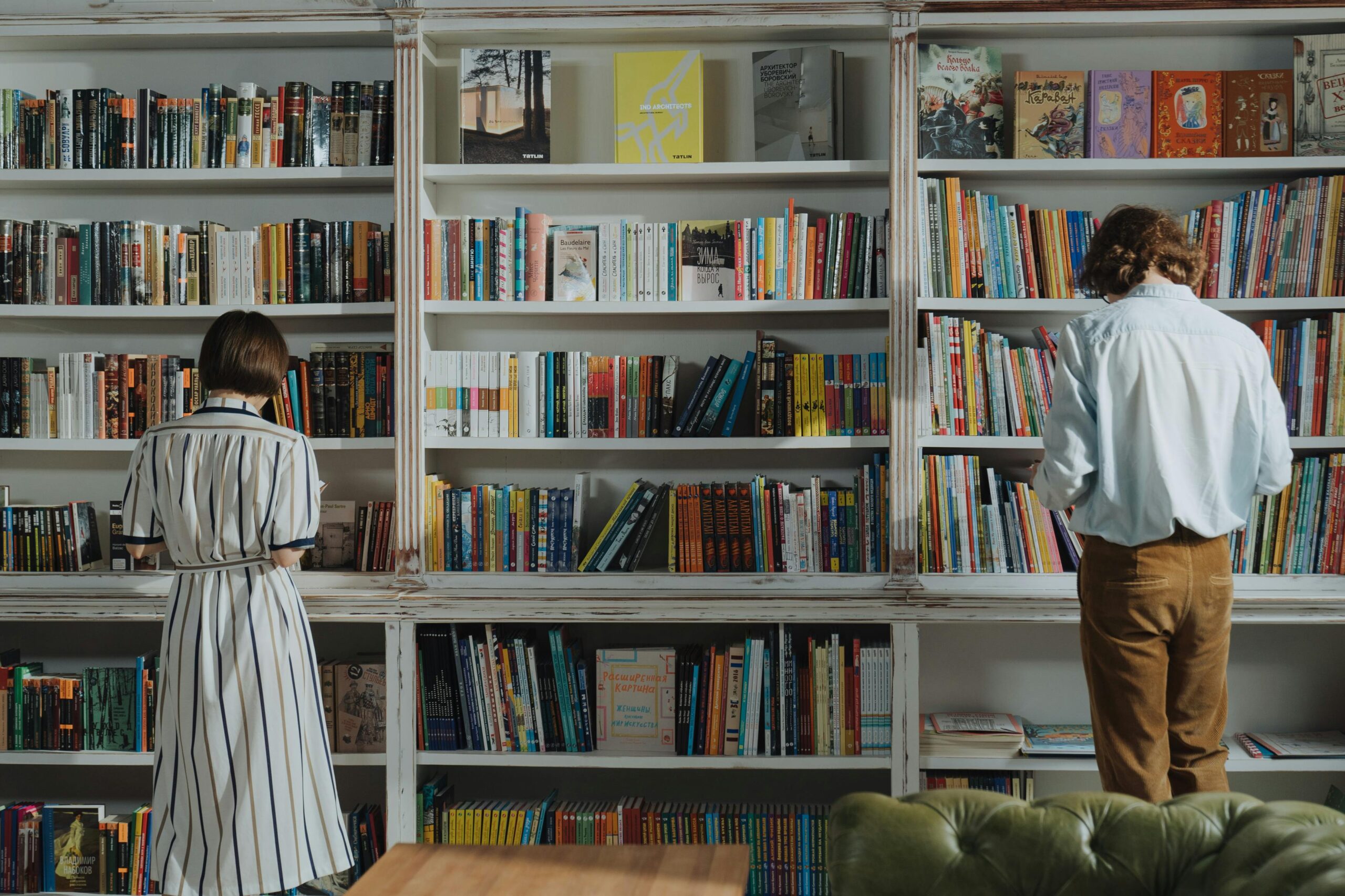 Bookshelf filled with colorful books and two individuals looking at the shelves.