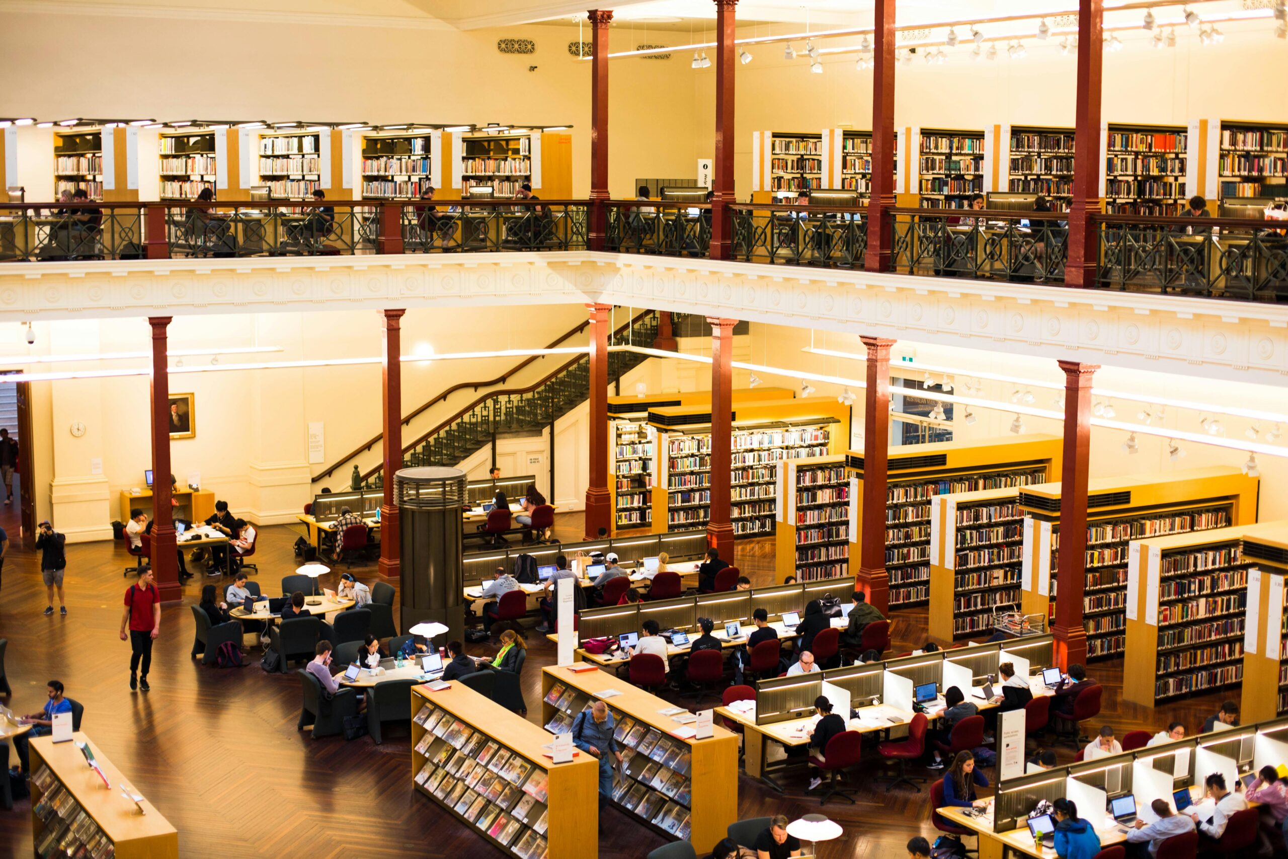 Library with multiple readers studying and researching with computers and bookshelves.