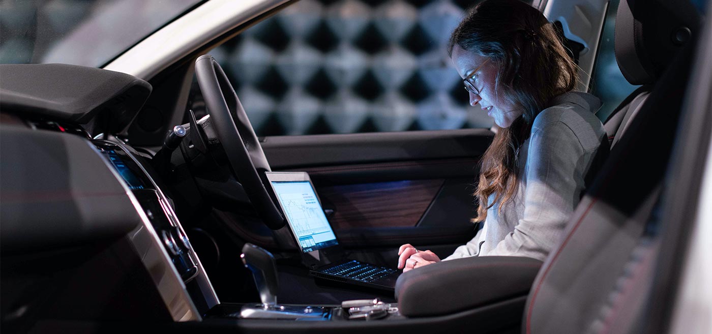 An individual working on automotive research using a laptop inside an autonomous vehicle.