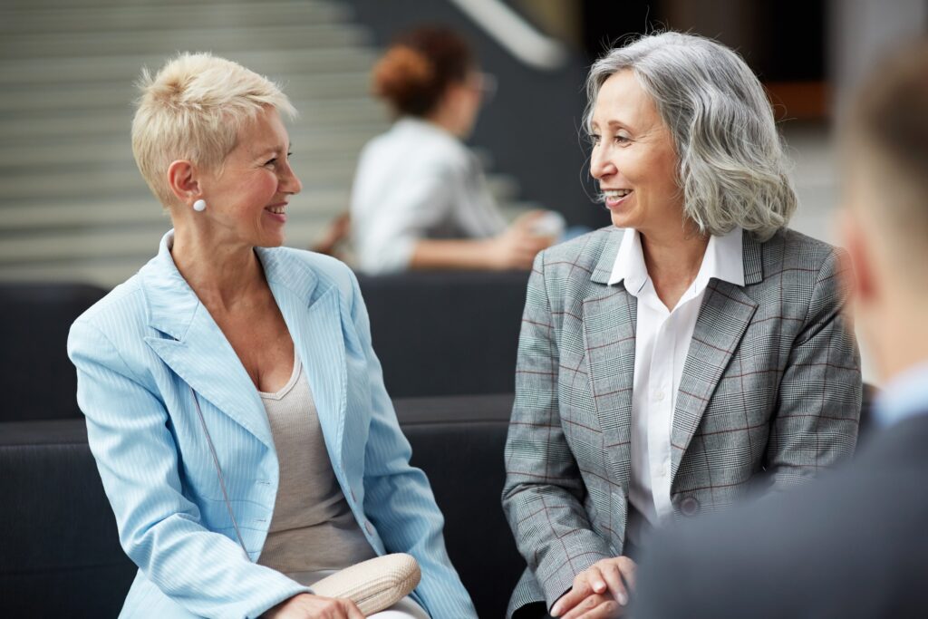 Smiling women engaging in conversation at a professional event, demonstrating networking and collaboration in business environments.