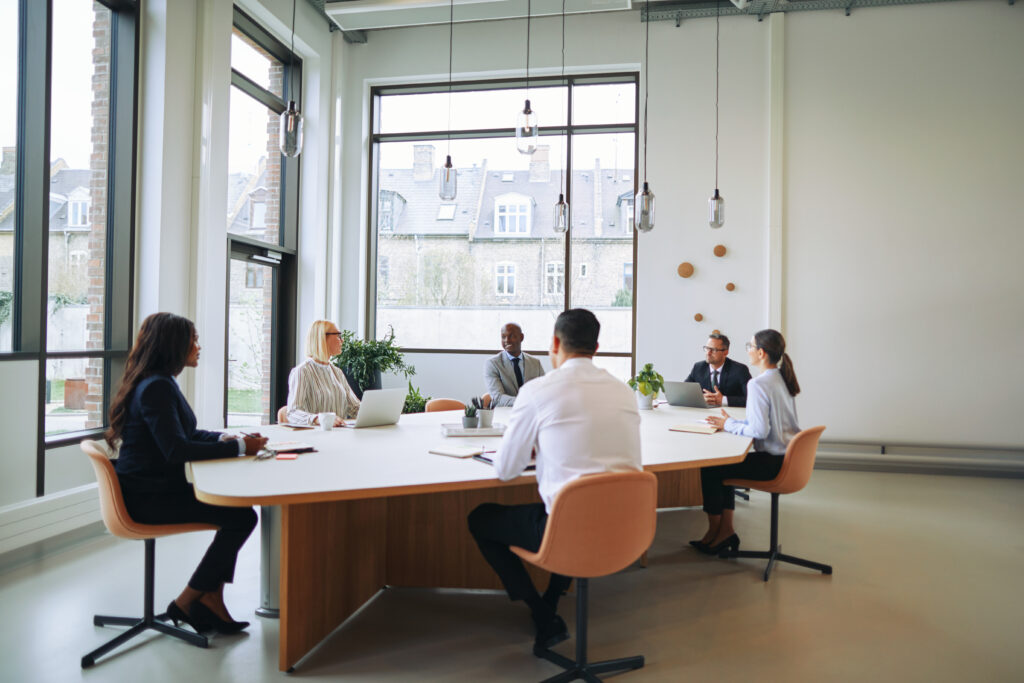 Diverse team of professionals engaging in a research discussion during a meeting in a well-lit, modern conference room.