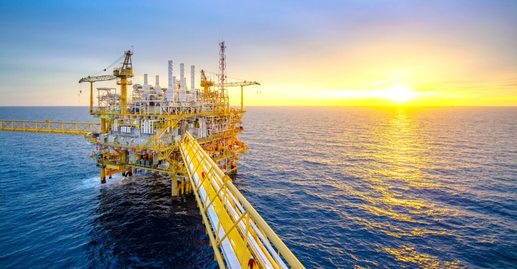 Offshore oil platform at sunset with vibrant sky background.