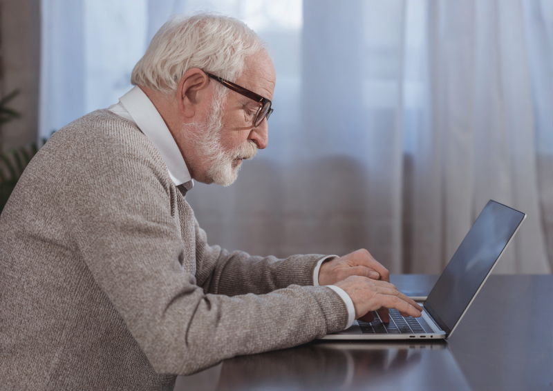Elderly man working on a laptop for academic research and scholarly pursuits.