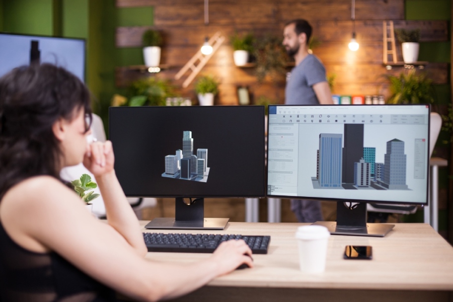 Architectural models and digital cityscape designs on computer screens in a creative workspace.